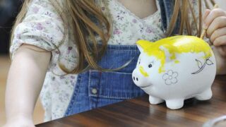 Junges Mädchen bemalt ein Sparschwein