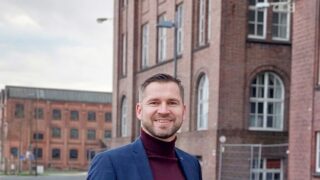 Ein Mann lächelt. Steht vor denkmalgeschützten Gebäude